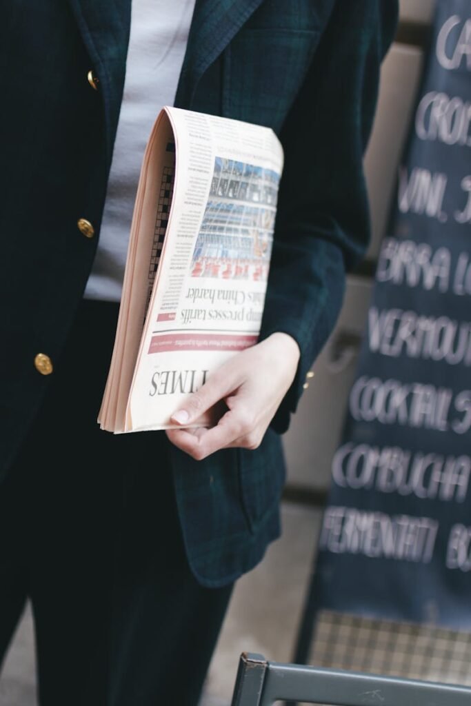 A business person in a suit holding a rolled-up newspaper outside a cafe.